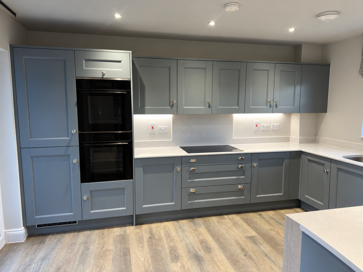 Blue-grey shaker kitchen with integrated ovens and pale stone worktops