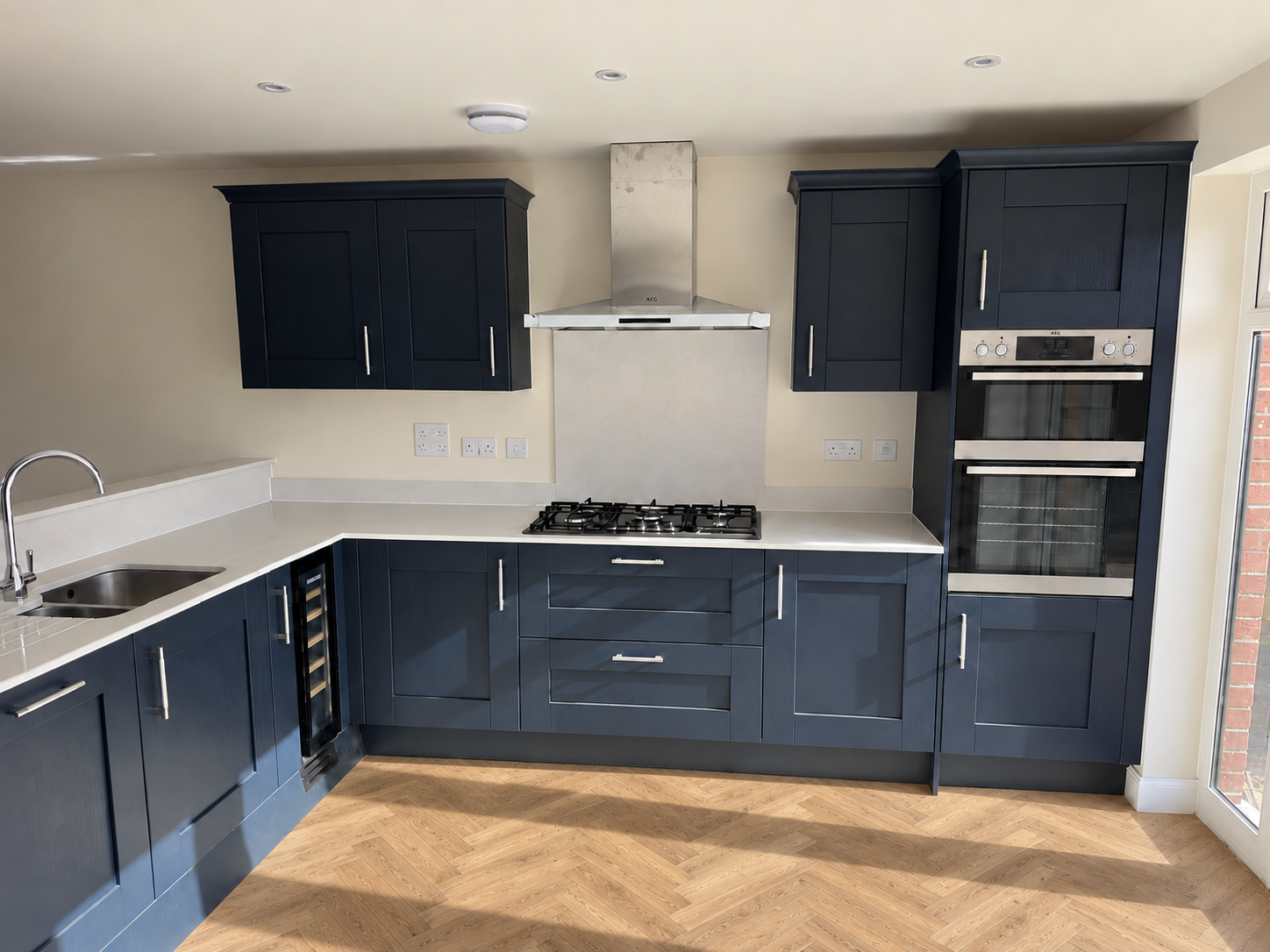 Deep navy fitted kitchen with gas hob, double ovens and herringbone floor