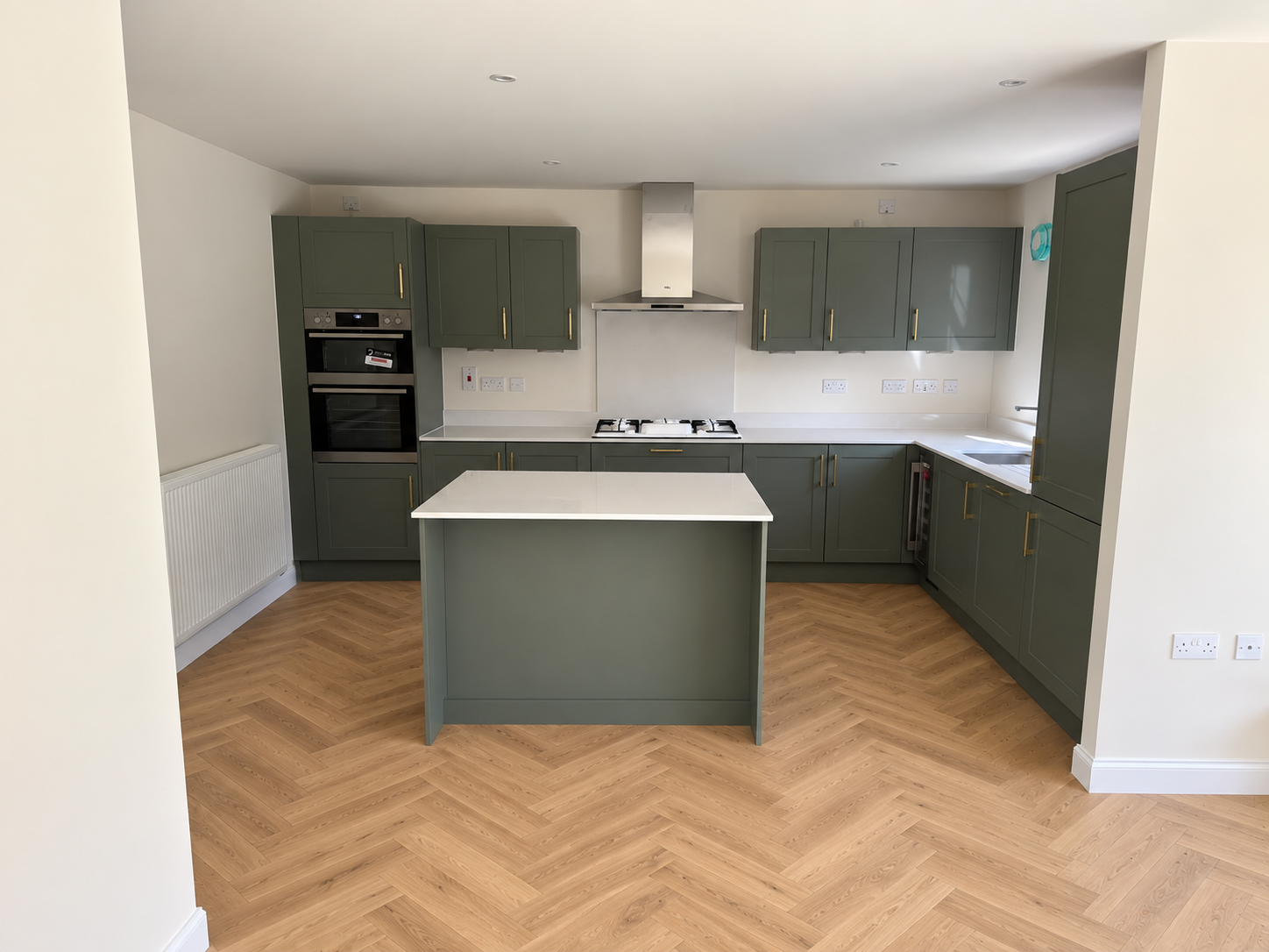 Sage green fitted kitchen with central island, brass handles and herringbone floor