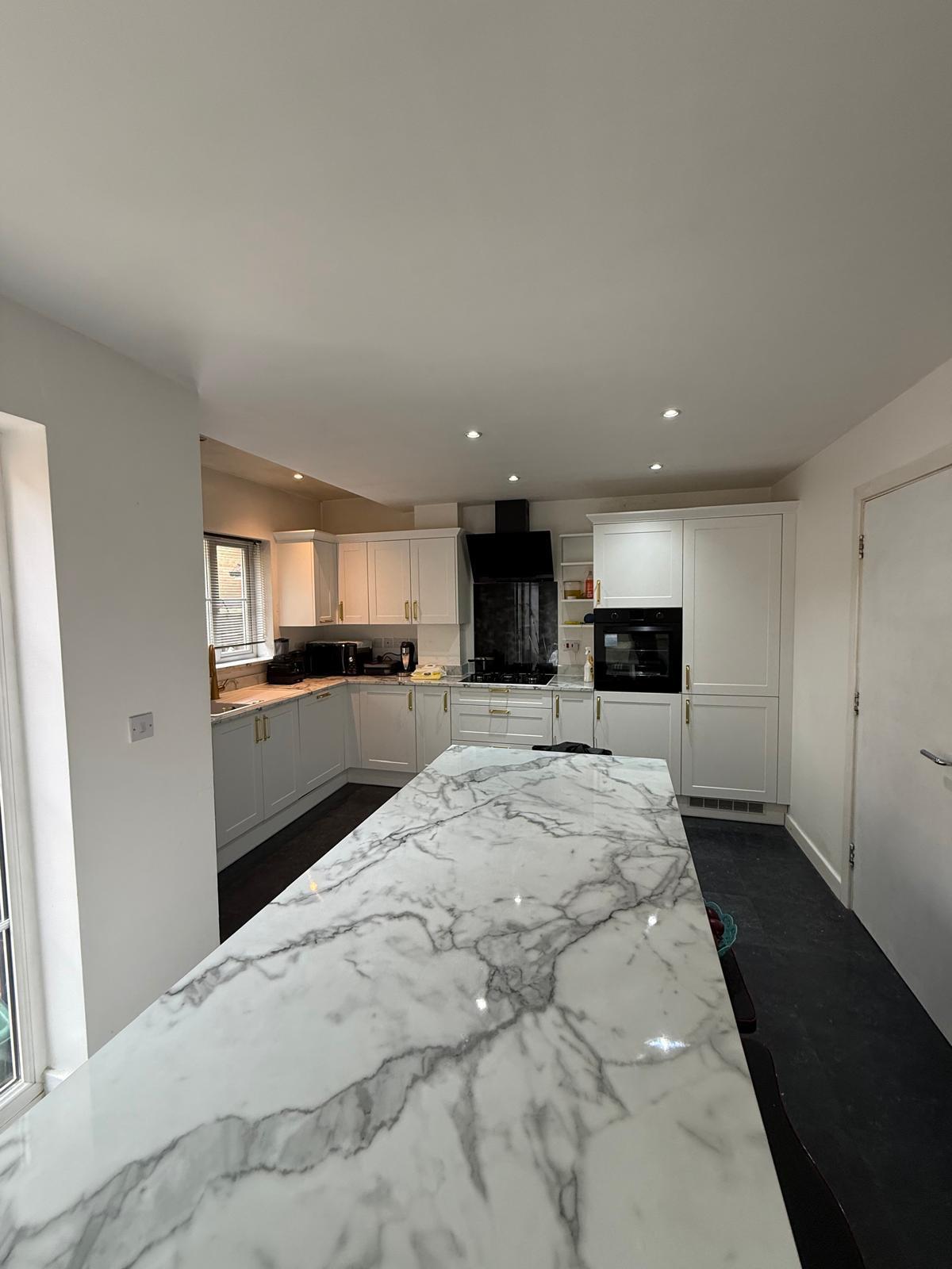 Finished white shaker kitchen with marble-effect island and brass handles
